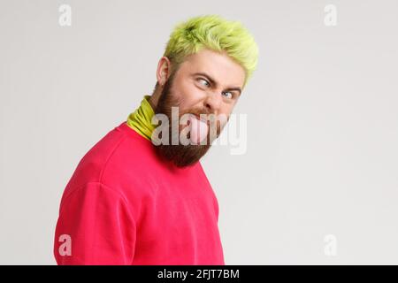 Foto di giovane bel pazzo caucasico stupido uomo, guarda la macchina fotografica con croci occhi e lingua fuori bocca, indossare pullover rosso, ha capelli gialli. Indù Foto Stock