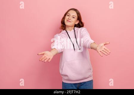 Ritratto di giovane donna gentile con capelli ricci che allungano le mani come se donare per libero, offrendo di abbracciare, invitante con espressione ospitale. IND Foto Stock