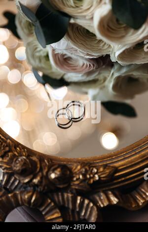 Anelli di nozze della sposa e dello sposo su una superficie di specchio con boke vicino fiori freschi. Celebrazione del matrimonio e preparazione. Foto Stock