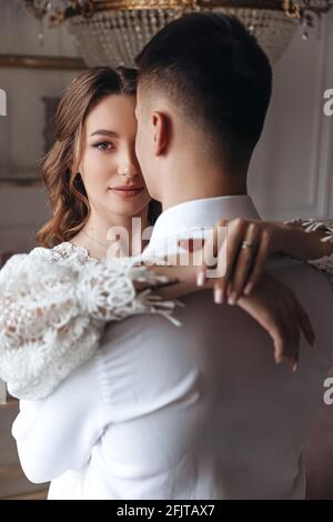 Una giovane sposa in un abito in pizzo abbraccia lo sposo. Sessione di foto di matrimonio di una coppia felice. Foto Stock