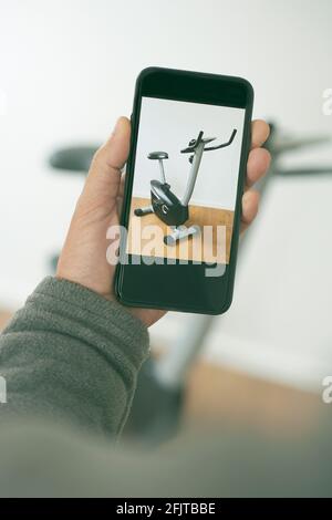 closeup di un giovane uomo caucasico che prende una foto con il suo smartphone della sua bicicletta stazionaria usata, per venderla o scambiarla su un marketpla online Foto Stock