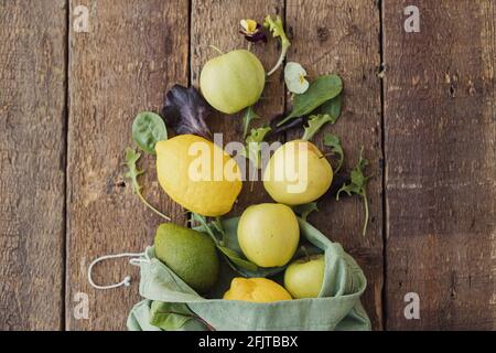 Concetto di shopping ecologico a zero rifiuti. Mele fresche, limone, avocado, foglie di insalata sparse da sacchetto di cotone eco su legno rustico. Ingredienti per insalate. Foto Stock