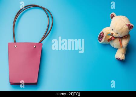 Una borsa regalo di carta rosa e un giocattolo orsacchiotto su sfondo blu. Una vista dall'alto con spazio da copiare. Vuoto per un biglietto di auguri. Derisione Foto Stock