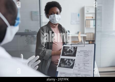 Medico che detiene un documento medico con immagine radiologica e che dà consigli alla donna incinta durante la sua visita in ospedale Foto Stock