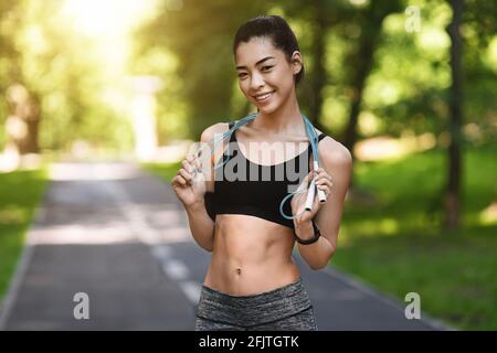 Donna modello di idoneità Asiatica sorridente che posa con corda saltante all'aperto Foto Stock