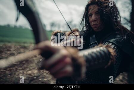 Donna in immagine di guerriero medievale arciere spara un arco e mira a bersaglio tra la foresta. Foto Stock