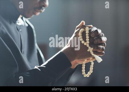 Primo piano di un uomo africano che tiene perle nelle sue mani e. pregare nella chiesa Foto Stock
