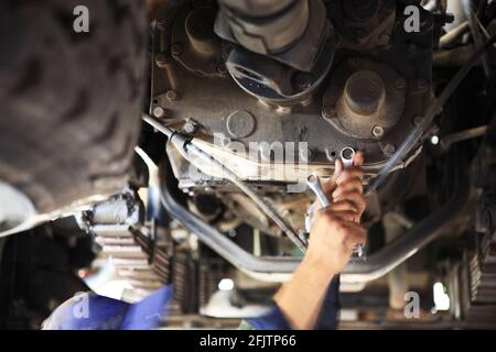 Un meccanico del motore sta lavorando su un cambio sotto un autocarro per merci pesanti in una fossa di un'officina con una chiave a bussola. Foto Stock