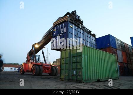 Il sollevamento e l'impilamento dei contenitori di carico in un cantiere di sera. Foto Stock