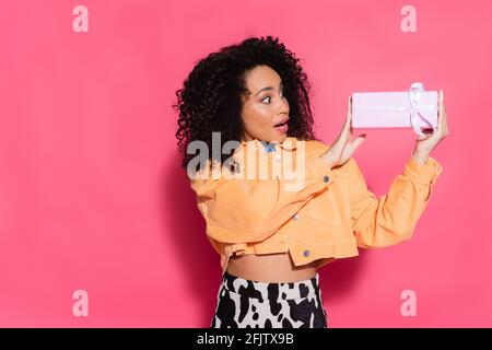 sorpresa afroamericana donna in giacca che tiene presente su rosa Foto Stock
