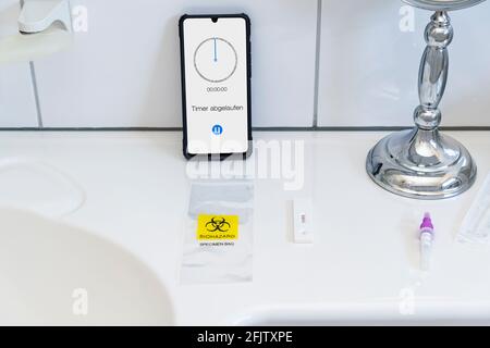 Un test dell'antigene SARS COV-2 è stato eseguito in un bagno. L'autotest Corona indica un risultato negativo del test. La striscia di prova si trova davanti a uno smartpho Foto Stock