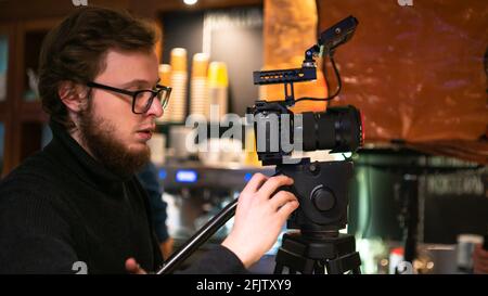 L'operatore professionale utilizza una fotocamera sul treppiede per impostare un cornice nel caffè Foto Stock