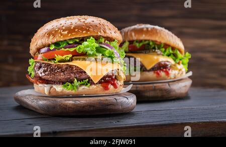 Deliziosi due hamburger su un tavolo di legno con sfondo marrone scuro dietro. Concetto di fast food. Foto Stock