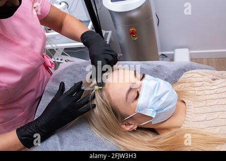 Donna che riceve iniezione in cuoio capelluto, mesoterapia, terapia di perdita dei capelli. Medici che indossano guanti in salone facendo manipolazioni mediche al paziente. Foto Stock