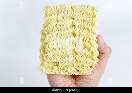 mano che tiene crudo spaghetti istantanei, sfondo bianco Foto Stock