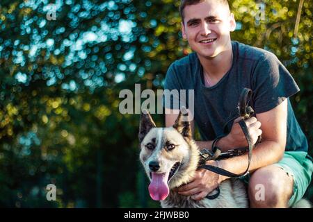 Immagine ritagliata del bel giovane uomo con il cane Husky siberiano all'aperto. Uomo su un'erba verde con cane. Cinologo. Concetto di amicizia. Millennial in un Foto Stock