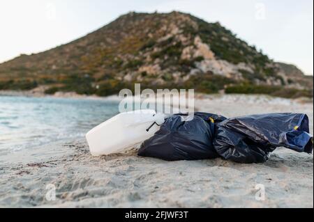 Sacchi pieni di rifiuti e contenitori di plastica giacenti sulla sabbia in una spiaggia dopo aver pulito la spiaggia. Lavoro volontario contro l'inquinamento e la contaminazione degli oceani Foto Stock