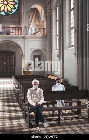Persone in maschere seduti sulla panchina in vecchio bello chiesa e preghiera Foto Stock