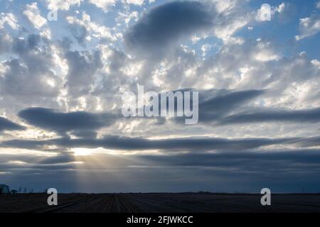 La luce di un sole che tramonta si rompe attraverso le nuvole serali su un campo agricolo invernale. Foto Stock