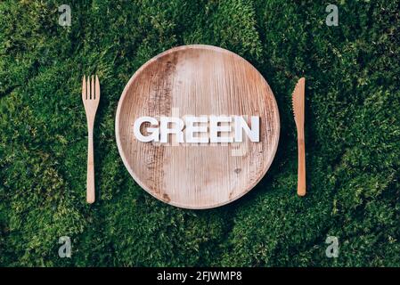 Stoviglie monouso in legno di materiali naturali con parola VERDE, cucchiaio di legno, forchetta su fondo di muschio verde. Stile di vita sostenibile ed ecologico Foto Stock