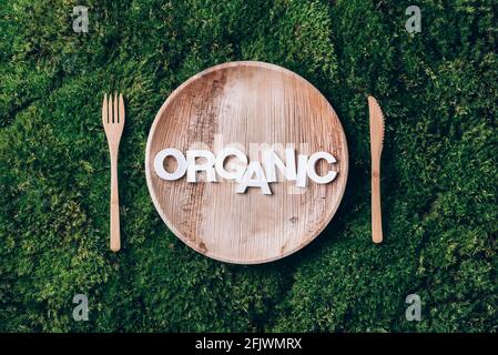 Stoviglie monouso in legno di materiali naturali con parola ORGANICA, cucchiaio di legno, forchetta su fondo di muschio verde. Stile di vita sostenibile ed ecologico Foto Stock