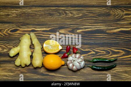 zenzero con limoni, aglio, peperoncino su fondo di legno Foto Stock