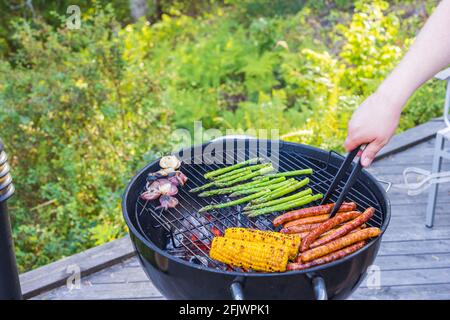 Vista ravvicinata delle mani dell'uomo che grigliano gli alimenti sulla griglia a carbone. Svezia. Foto Stock