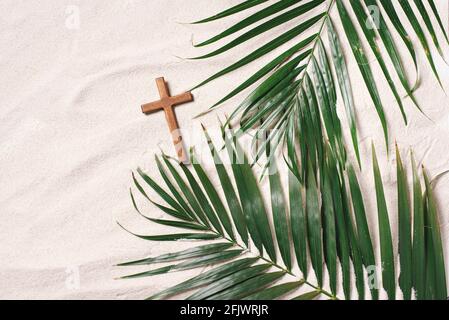 Concetto di domenica delle Palme. Croce fatta di palme e foglie tropicali su sfondo di sabbia. Festa cristiana movibile per celebrare l'ingresso trionfale di Gesù in Foto Stock