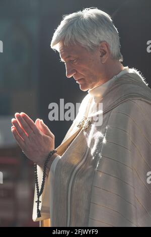 Sacerdote senior che tiene perline di rosario e prega durante la cerimonia in la chiesa Foto Stock