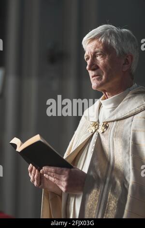 Sacerdote anziano in piedi con la Bibbia e la lettura delle preghiere durante il matrimonio nella chiesa Foto Stock