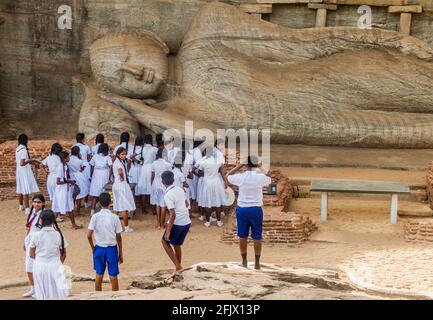 POLONNARUWA, SRI LANKA - 22 LUGLIO 2016: I bambini nelle uniformi scolastiche visitano la statua del Buddha reclinata al tempio di roccia di Gal Vihara nell'antica città di Polonn Foto Stock