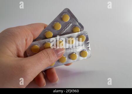 Due blister con pillole gialle in una mano femminile su uno sfondo chiaro. Farmaci orali Foto Stock