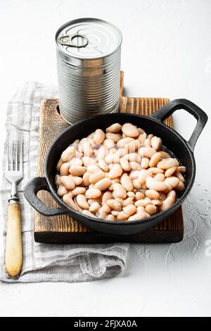 Set di fagioli bianchi in scatola, con lattina metallica, in padella di ghisa, su superficie di pietra bianca Foto Stock