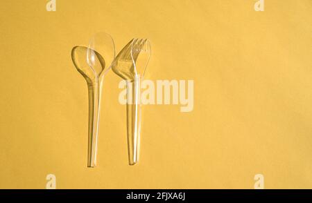 Cucchiaio trasparente e posate a forchetta con ombre, su sfondo giallo. Concetto di inquinamento o rifiuti in plastica. Foto Stock