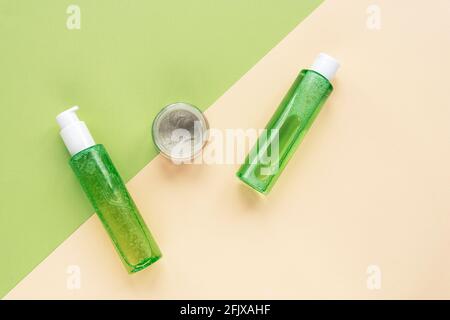 Bottiglie cosmetiche verdi con gel lavaviso, tonico e maschera facciale su sfondo beige e verde. Cosmetici naturali biologici. Vista dall'alto, disposizione piatta Foto Stock