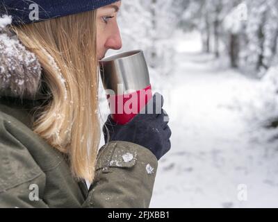 Il tè mantiene la ragazza calda all'esterno. Giovane donna che ama la bevanda calda in inverno. Abete rosso albero Foresta coperta da neve in inverno Paesaggio sullo sfondo . immagine per sfondo. Spazio di copia Foto Stock