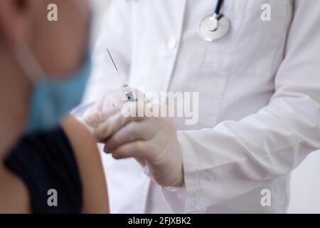 Medico femminile che tiene la siringa e che usa il cotone prima di fare l'iniezione al paziente in maschera medica. Vaccino Covid-19 o coronavirus Foto Stock