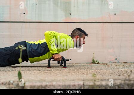 Vista laterale di un giovane uomo bruna che fa push-up con spingere verso l'alto le barre in un parcheggio Foto Stock