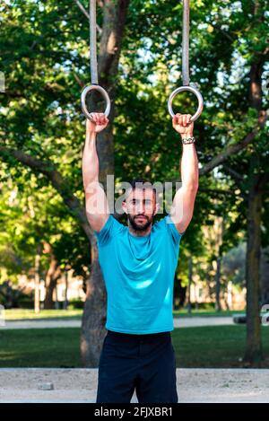 Atleta dai capelli scuri con barba che si tiene sugli anelli da ginnastica. Foto Stock