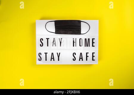 Lightbox STAY HOME RESTA AL SICURO su sfondo giallo con nero maschera protettiva Foto Stock