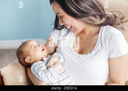 Madre asiatica che tiene dondolo bambino neonato figlio. Stile di vita domestico Foto Stock