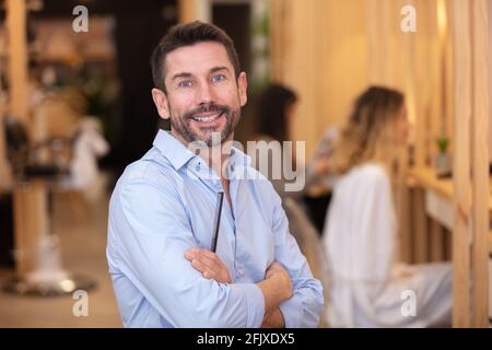 sorridente parrucchiere maschile in posa in salone Foto Stock