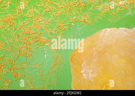 cucinando gli spaghetti fatti in casa su un tavolo verde delle fette pasta tagliata in strisce e un cerchio laminato grezzo fatto dalla farina di grano senza glutine, aggiungere in primo piano Foto Stock
