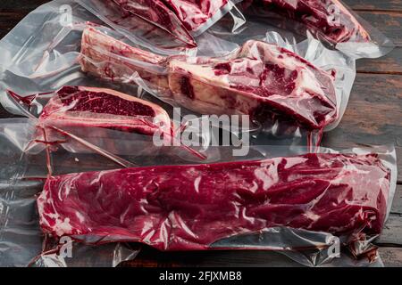 Carne di manzo cruda nel set di impacchi sottovuoto, tomahawk, t bone, bistecca di club, costolette e tagli di filetto, su sfondo vecchio tavolo di legno scuro Foto Stock