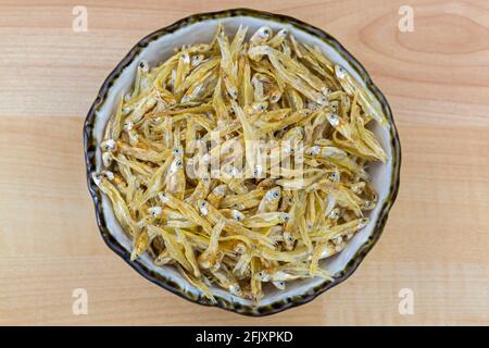 Anchovy essiccato in recipiente di ceramica. Acciughe piccolo pesce, vista dall'alto di sfondo in legno Foto Stock