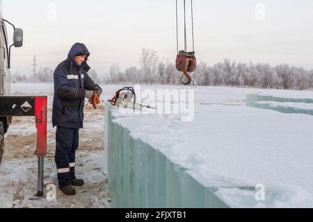 Un installatore mette un guanto sulla sua mano destra sullo sfondo di blocchi di ghiaccio, una motosega e un carrello elevatore Foto Stock