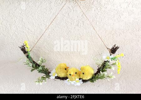 Decorazione della molla, 3 piccoli pulcini falsi gialli seduti su un'oscillazione di ramo fatta di ramoscelli e fiori piccoli su sfondo bianco, tempo di Pasqua. Spazio di copia Foto Stock