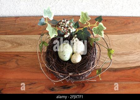 Illustrazione della molla. 3 uova colorate piccole in un nido di pino per Pasqua, foglie verdi e ramoscelli tutto intorno su tavola di legno Foto Stock