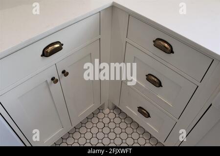 Angolo cucina con piano di lavoro bianco e armadi e pavimenti in piastrelle testurizzate. Piccole maniglie in bronzo vintage per l'apertura e la chiusura delle porte. Casa colonica Foto Stock