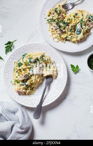 Spaghetti al tonno, spinaci e salsa cremosa su un piatto bianco con erbe, fondo in marmo bianco. Foto Stock
